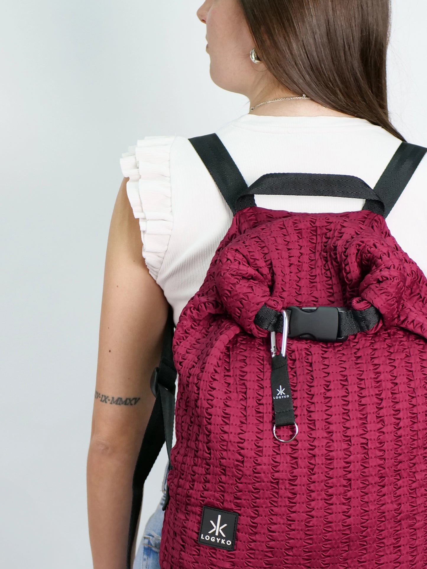 Dettaglio ravvicinato dello zaino LOGYKO modello Hydrogen in Bordeaux, indossato da una persona. Si vedono la chiusura rolltop con fibbia di gomma e il portachiavi con moschettone metallico attaccato alla chiusura dello zaino.
Tessuto riciclato 3D bordeaux, design urbano e sostenibile, ideale per l’uso quotidiano.