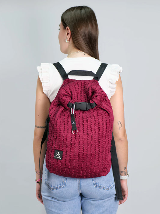 Persona di spalle che indossa lo zaino LOGYKO modello Hydrogen nel colore Bordeaux, realizzato in tessuto riciclato con trama 3D, chiusura rolltop e spallacci regolabili. Design urbano e sostenibile, ideale per la vita quotidiana.