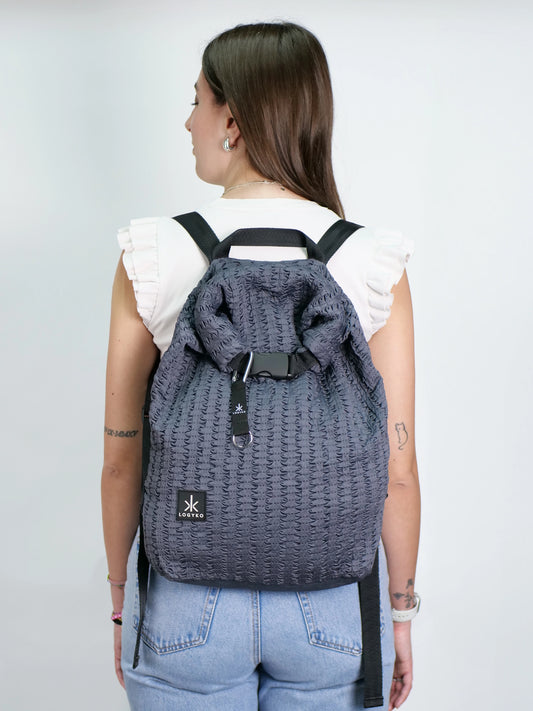 Persona di spalle che indossa lo zaino LOGYKO modello Hydrogen nel colore Dark Grey, realizzato in tessuto riciclato con trama 3D, chiusura rolltop e spallacci regolabili. Design urbano e sostenibile, perfetto per affrontare la routine quotidiana con stile.