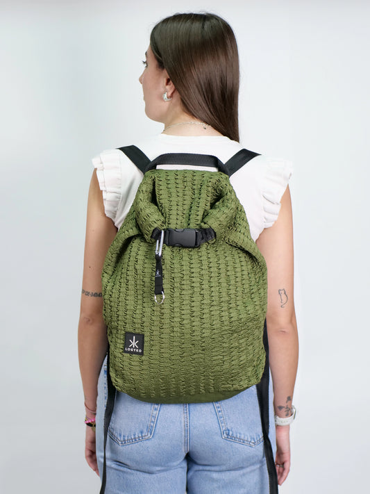 Persona di spalle che indossa lo zaino LOGYKO modello Hydrogen in Military Green, realizzato in tessuto riciclato 3D, con chiusura rolltop e spallacci regolabili. Design urbano e sostenibile, ideale per la vita quotidiana.